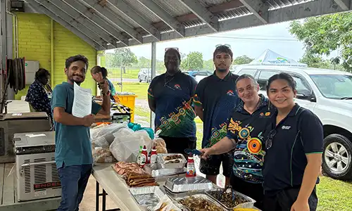 6 people stand behind a food table at Belyuen Groove Festival